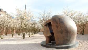 Bronzeskulptur „Figure in a Shelter“ von Henry Moore im Skulpturenpark Vaduz – umgeben von blühenden Bäumen im Frühling.