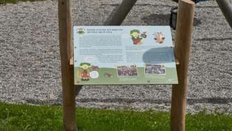 Zwei Kinder betrachten gemeinsam eine Erlebnisstation und lernen auf dem interaktiven Naturpfad „Wurz und Zirp auf Zeitreise“ über Tiere und Pflanzen in Liechtenstein.