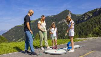 Familie spielt gemeinsam Minigolf in den Bergen von Malbun bei strahlendem Sonnenschein