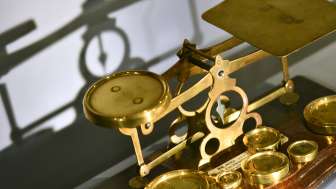 Bild einer antiken goldfarbenen Balkenwaage mit verschiedenen Gewichten, ausgestellt im Liechtensteinischen PostMuseum