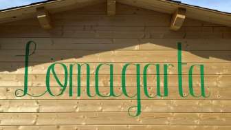 Ansicht auf das grüne Lömagarta-Logo, das stilvoll auf der Holzfassade des gemütlichen Biergartens prangt.