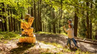 Zwei Wanderer laufen an einer Holzfigur auf dem WalserSagenWeg vorbei