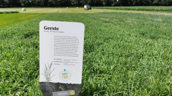 Tafel mit Informationen auf dem Weltacker Balzers mit grünen Feld im Hintergrund