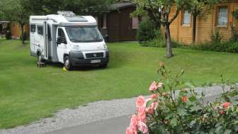 Wohnmobilstellplatz auf dem Campingplatz Mittagsspitze mit grüner Wiese und umgebenen Holzhütten.