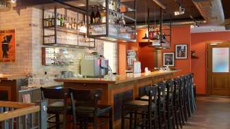oderne Bar im New Castle Vaduz mit langer Holztresen, hohen Stühlen und hängenden Glasregalen in warmem Ambiente.