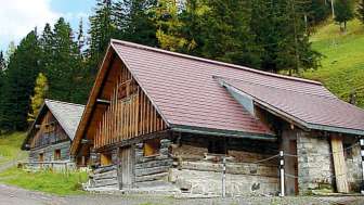 Historisches Holzgebäude des alten Jugendheims in Malbun vor bewaldetem Berghang.