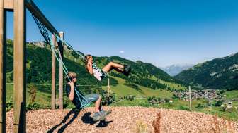Zwei Kinder schaukeln mit der Aussicht auf Malbun