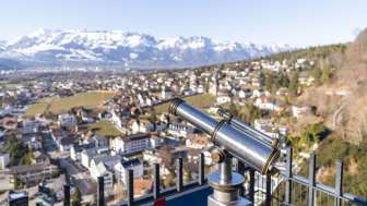 Fernrohr am Schlossweg-Aussichtspunkt Känzile mit Blick auf Vaduz und das verschneite Alpenpanorama im Hintergrund.