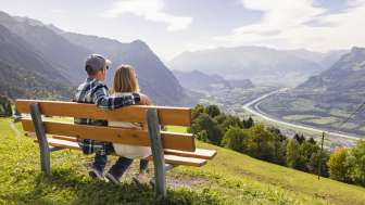 Zwei Wanderer sitzen auf einer Bank und geniessen die Aussicht auf das Rheintal