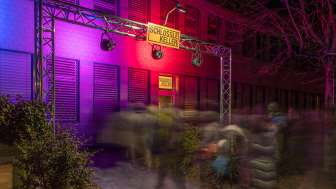 Eingangsbereich des Kleintheaters Schlösslekeller bei Nacht mit farbiger Beleuchtung und Publikum