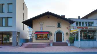Außenansicht des Alten Kino Vaduz mit Schriftzug über dem Eingang und roten Markisen, zwischen zwei modernen Gebäuden gelegen.