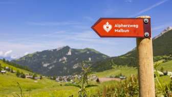 Wegweiser Alpherzweg mit Bergdorf Malbun im Hintergrund