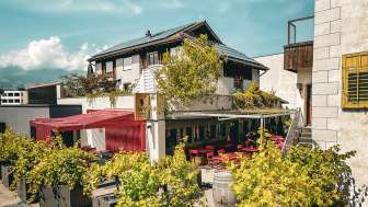 Gemütlicher Außenbereich der WY Weinbar mit sonniger Terrasse und üppiger Bepflanzung vor traditioneller Fassade in Liechtenstein.