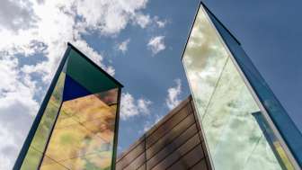 Kunstinstallation „Zwei Licht-Prismen“ von Heinz Mack mit farbig schimmernden Glasflächen vor blauem Himmel.