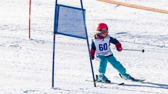 Kleines Kind mit Startnummer fährt konzentriert beim Kinderskirennen im malbi-park durch die Tore