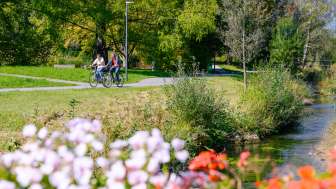 Radfahrer genießen das sonnige Wetter entlang des mit Blumen gesäumten Ufers im Naturpark Haberfeld.