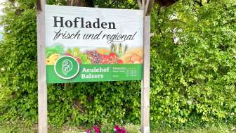 Schild des Hofladens Aeulehof mit Aufschrift „Frisch und regional“ vor grüner Hecke in Triesen.